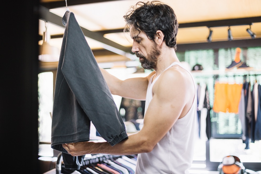 Man inspecting black jogger pants in a clothing store, checking fabric and quality of best gym wears activewear