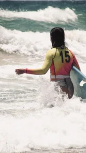 Surfer wearing a red and black rash guard while riding waves in the ocean.
