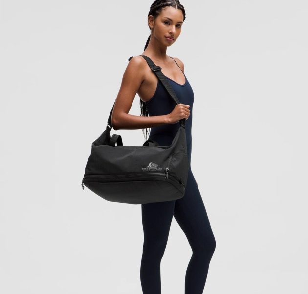 Woman carrying black gym duffel bag over shoulder.
