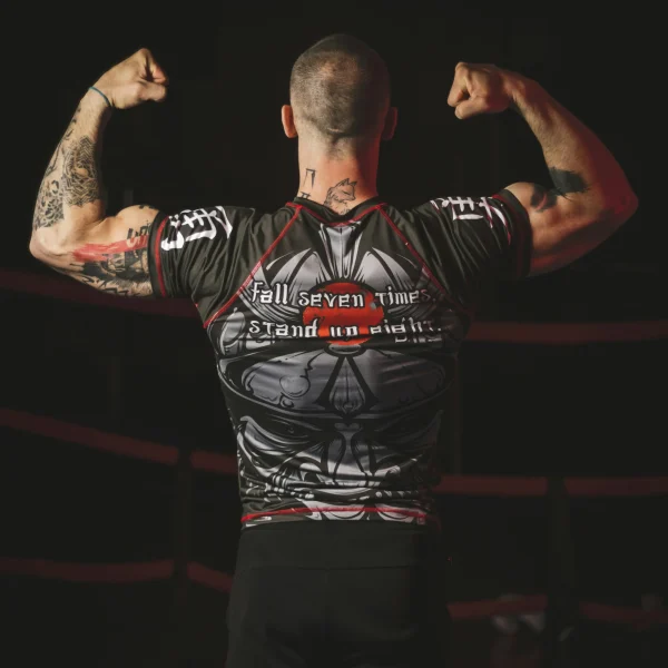 Male athlete wearing a black short-sleeve custom rash guards and flexing inside a combat sports ring.